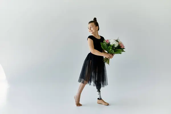 A young girl with a prosthetic leg, wearing a black leotard and skirt, holds a bouquet of flowers while smiling. — Stock Photo