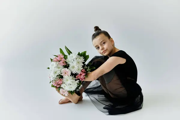A young girl with a prosthetic leg, wearing a black leotard, sits with a bouquet of flowers. — Stock Photo