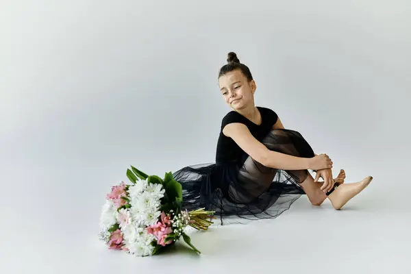 A young girl with a prosthetic leg sits on the floor in a black leotard and tutu, holding a bouquet of flowers. — Stock Photo