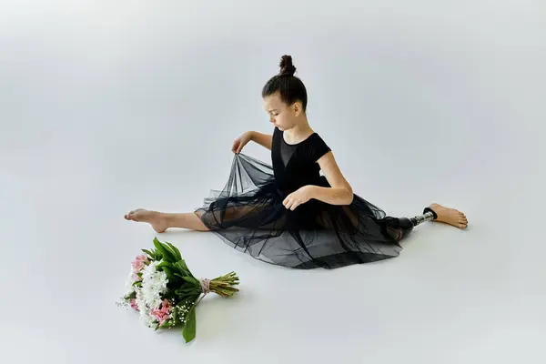 A young girl with a prosthetic leg performs a graceful gymnastics stretch in a black leotard and tutu. — Stock Photo