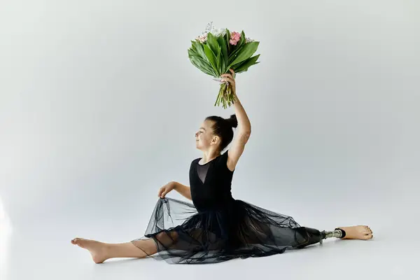 A young girl with a prosthetic leg performs a gymnastic split while holding a bouquet of flowers. — Stock Photo