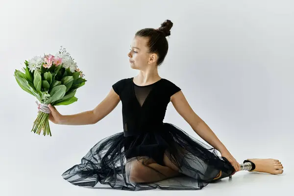A young girl with a prosthetic leg poses gracefully in a black leotard and tutu, holding a bouquet of flowers. — Stock Photo