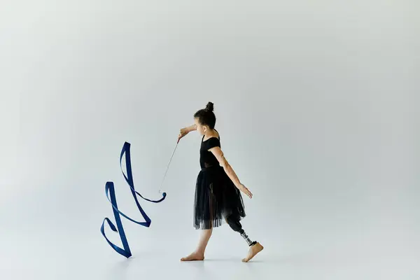 A young girl with a prosthetic leg performs gymnastics with a blue ribbon in a white studio. — Stock Photo