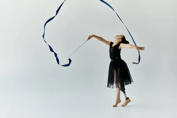 A young girl with a prosthetic leg performs rhythmic gymnastics with a blue ribbon. — Stock Photo