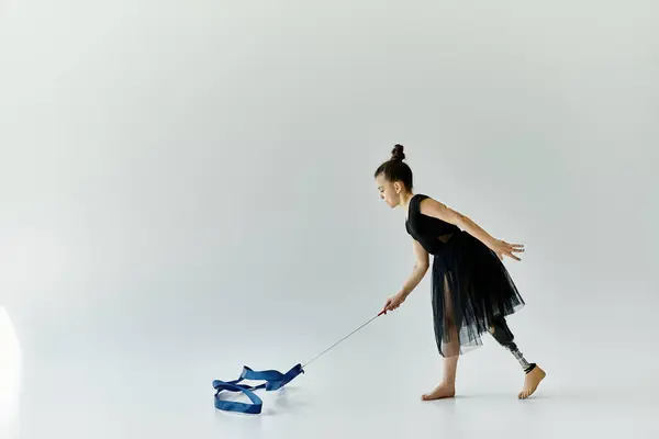 A young girl with a prosthetic leg performs a graceful ribbon routine in a white studio. — Stock Photo