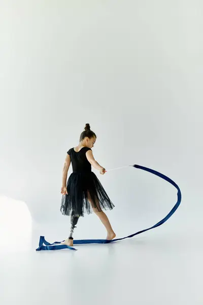 A young girl with a prosthetic leg performs a gymnastics routine with a blue ribbon. — Stock Photo