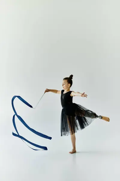 A young girl with a prosthetic leg performs a rhythmic gymnastics routine with a blue ribbon. — Stock Photo