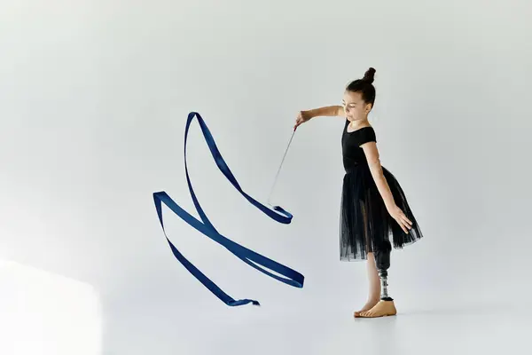 A young girl with a prosthetic leg practices rhythmic gymnastics, skillfully manipulating a blue ribbon. — Stock Photo