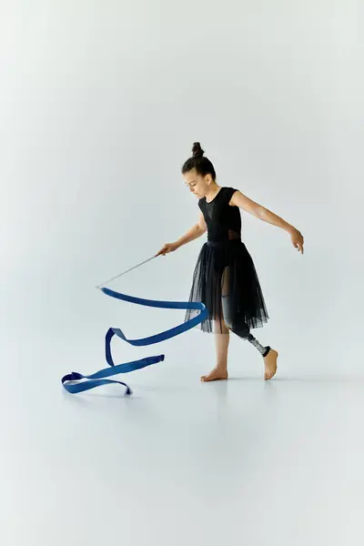 A young girl with a prosthetic leg performs gymnastics with a blue ribbon. — Stock Photo