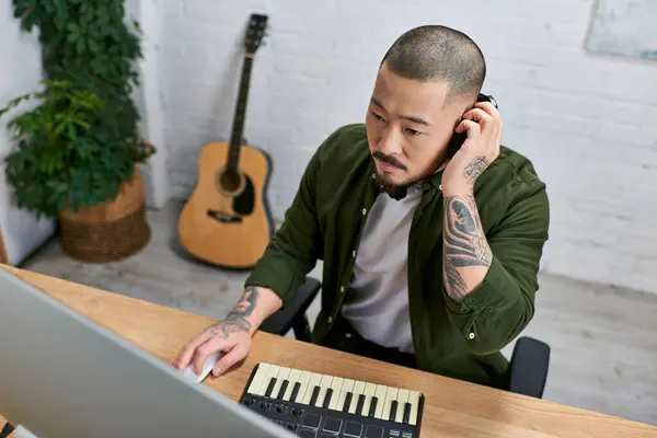 Un hombre asiático guapo toca un teclado y trabaja en un ordenador en un entorno de estudio. - foto de stock
