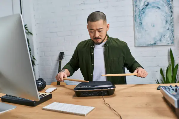 A young Asian man in a casual green shirt plays a drum pad in his studio. — Stock Photo