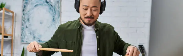 A handsome Asian man in casual attire plays a musical instrument in his studio. — Stock Photo