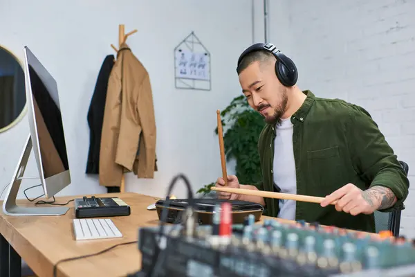 A handsome Asian man plays drums in a casual setting while wearing headphones. — Stock Photo