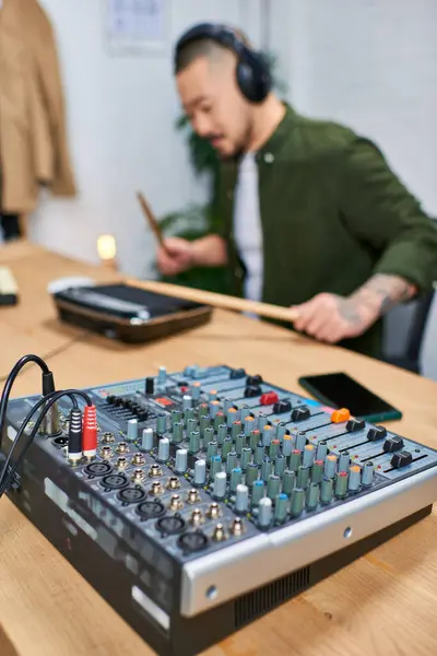 Крупный план звукового миксера в студии с размытым изображением азиата, играющего на инструменте на заднем плане. — стоковое фото