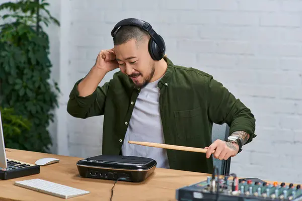 Ein junger asiatischer Mann mit Kopfhörer spielt in einem Tonstudio ein Schlagzeug. — Stock Photo