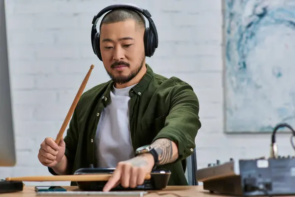 A handsome Asian man wearing headphones plays drums in a studio setting. — Stock Photo
