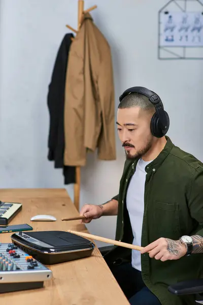 A young Asian man plays a drum pad while wearing headphones in a music studio. — Stock Photo