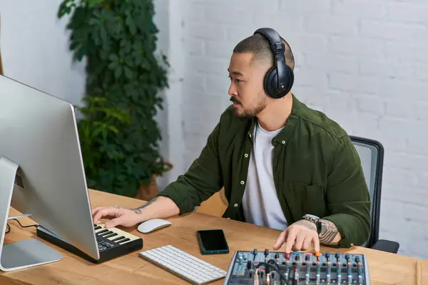 Ein gut aussehender asiatischer Mann, der Kopfhörer trägt, arbeitet in seinem Studio an einem Musikprojekt. — Stockfoto