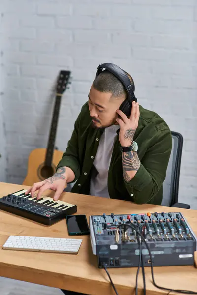 Ein Asiate spielt Keyboard in seinem Studio, im Hintergrund ein Mischpult und eine Gitarre. — Stockfoto