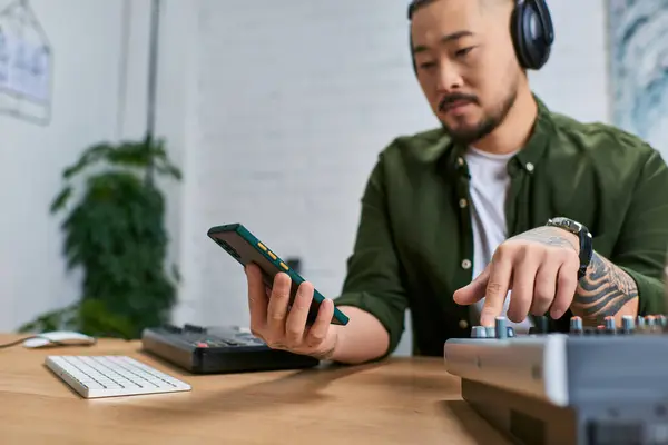 A young Asian man mixes music in his studio, wearing casual clothes, with a focused expression. — Stock Photo