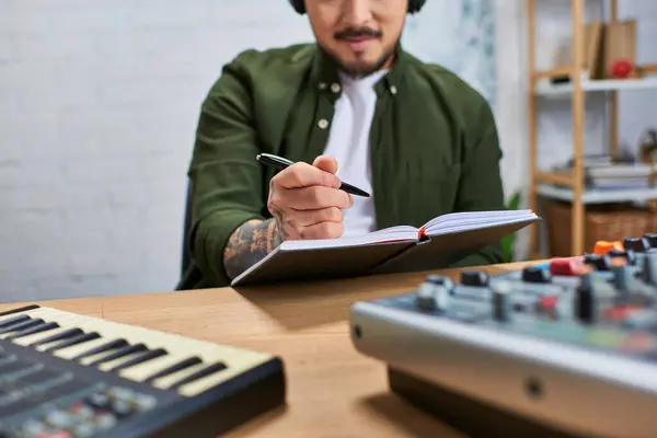An Asian man wearing casual attire works on a new musical piece in a recording studio. — Stock Photo