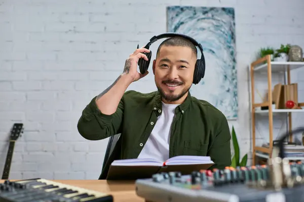 A handsome Asian man wearing headphones sits in his studio, smiling and looking at the camera. — Stock Photo
