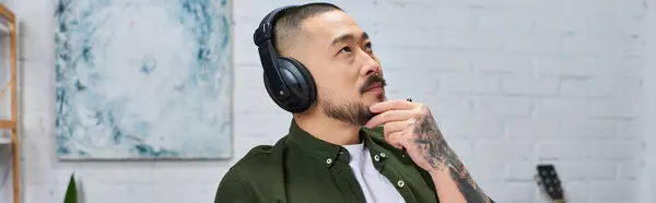 A handsome Asian man wearing headphones in a studio setting, lost in thought. — Stock Photo