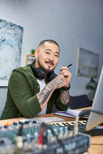 Un joven asiático en un estudio de grabación, auriculares alrededor de su cuello, con una pluma en la mano. - foto de stock