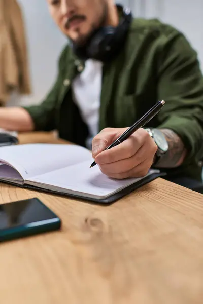 A close-up of an Asian man writing in a notebook, likely composing music in his studio. — Stock Photo