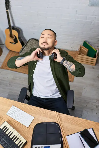 A young Asian man, dressed in casual clothes, takes a break from playing music in his studio. — Stock Photo