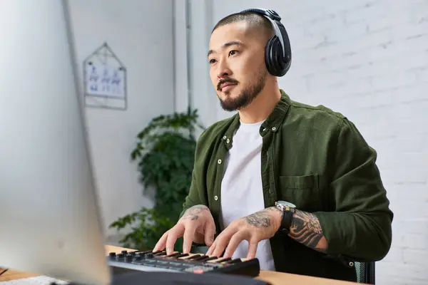 An Asian man with headphones plays a keyboard in his studio. — Stock Photo