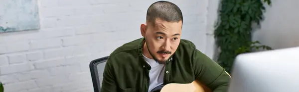 A handsome Asian man plays a guitar in a studio setting. — Stock Photo