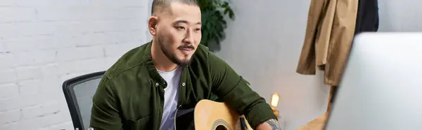 A handsome Asian man plays an acoustic guitar in a recording studio. — Stock Photo