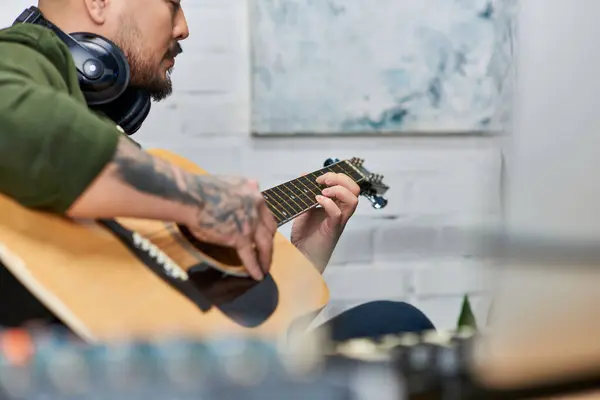 Ein gutaussehender asiatischer Mann mit Tätowierungen spielt in einem Tonstudio eine akustische Gitarre. — Stockfoto