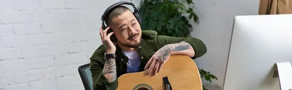An Asian man in casual clothing plays guitar in his studio. — Stock Photo