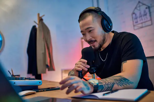 A handsome Asian man wearing headphones records a podcast in his studio. — Stock Photo