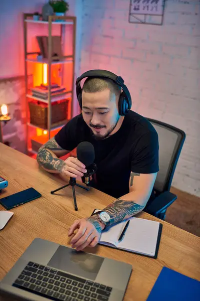 A handsome Asian man wearing headphones records a podcast in his home studio. — Stock Photo