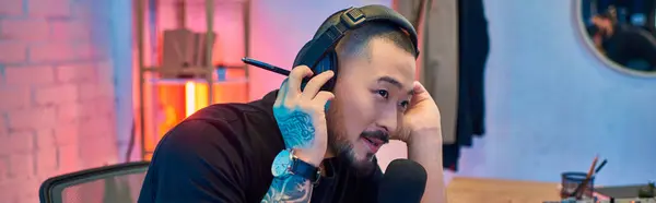 A young Asian man records a podcast in his studio, wearing headphones and a microphone. — Stock Photo