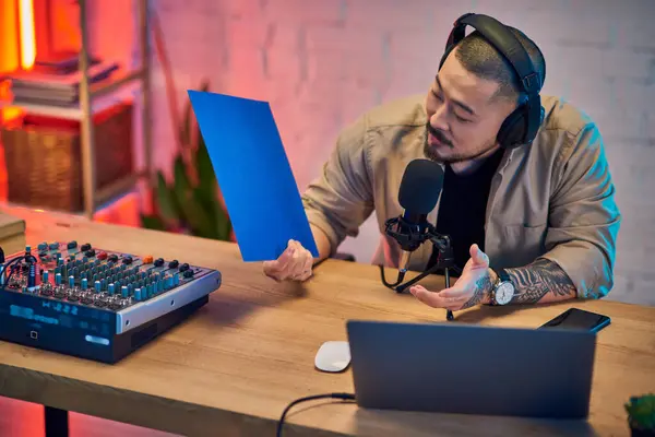 A handsome Asian man sits in his home studio, headphones on, recording a podcast with a microphone. — Stock Photo