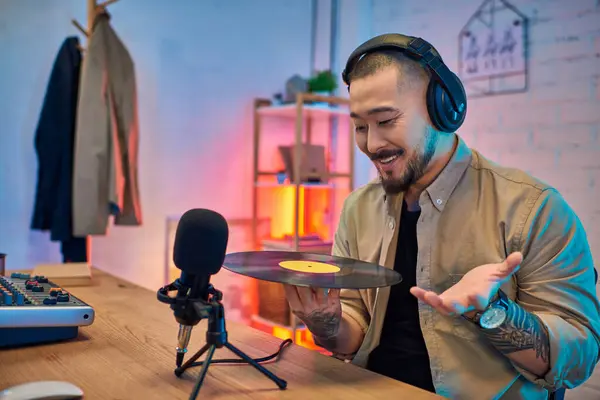Un bell'asiatico registra un podcast nel suo studio, tenendo un disco in vinile e parlando con entusiasmo in un microfono. — Foto stock