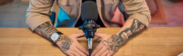 A handsome Asian man with tattooed arms sits in his podcast studio, preparing to record. — Stock Photo