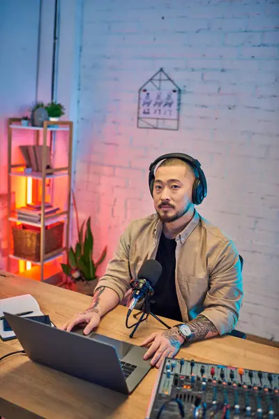 A handsome Asian man wearing headphones records a podcast in his home studio. — Stock Photo