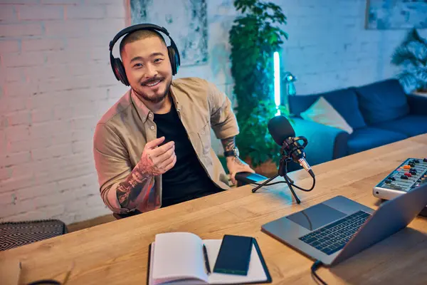 A smiling Asian man wearing headphones records a podcast in his studio. — Stock Photo