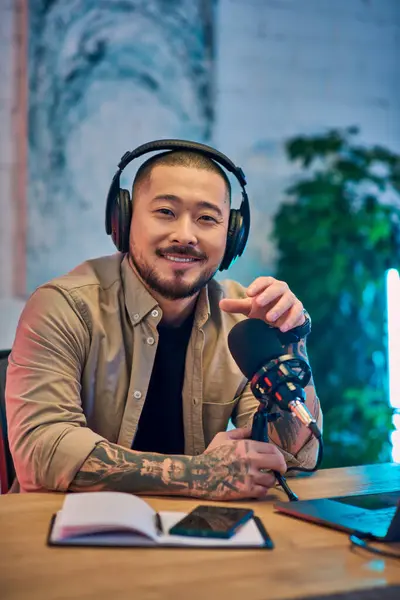 A handsome Asian man podcasting at his desk with headphones on. — Stock Photo