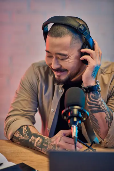 An Asian man smiles while podcasting in his studio. — Stock Photo