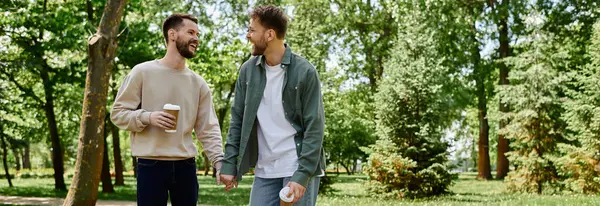 Una coppia gay barbuta cammina mano nella mano attraverso un parco in una giornata di sole, godendosi reciprocamente la compagnia. — Foto stock