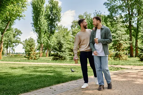 Un couple gay barbu marche main dans la main dans un parc verdoyant, profitant d'un après-midi ensoleillé ensemble. — Photo de stock