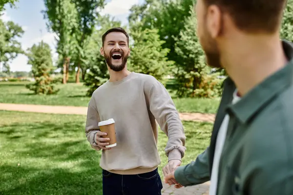 A bearded gay couple enjoys a sunny afternoon in the park, holding hands and laughing. — Stock Photo