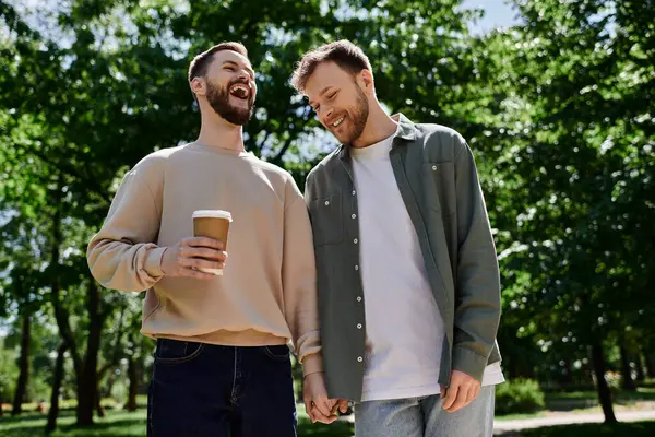 A bearded gay couple walks through a green park, laughing and enjoying each others company. — Stock Photo