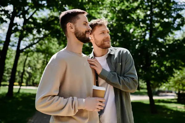 Un couple gay barbu profite d'une pause café dans un parc verdoyant, partageant un moment d'amour et d'intimité. — Photo de stock